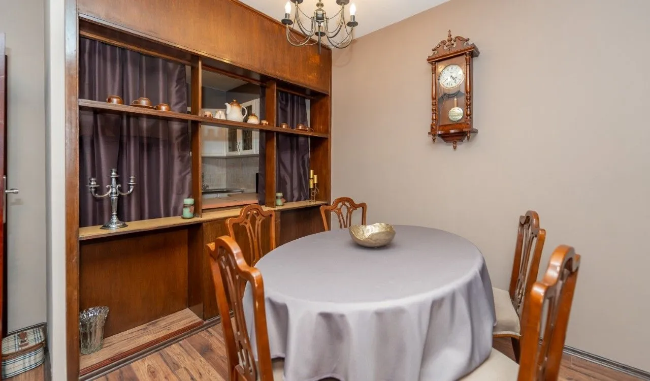 Dining area with a round table, wooden room divider shelf, and a wall clock.