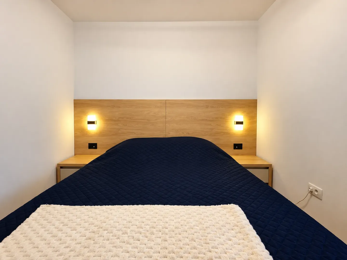 A bedroom featuring a double bed, a wooden headboard panel, and wall lamps.