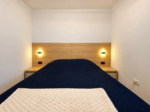 A bedroom featuring a double bed, a wooden headboard panel, and wall lamps. - image 5