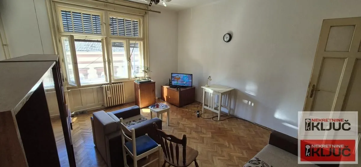 Dnevna soba sa garniturom za sedenje, televizorom i parketom na podu.