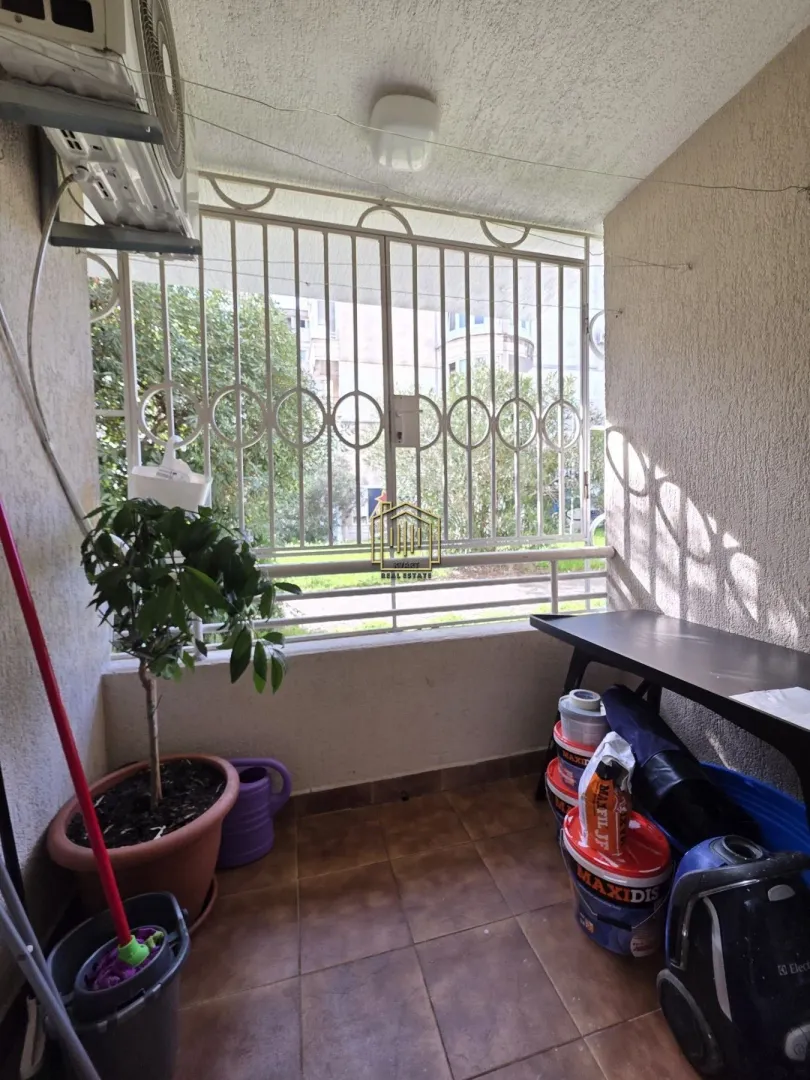 Manji zatvoreni balkon sa metalnom ogradom i saksijama sa biljkama.