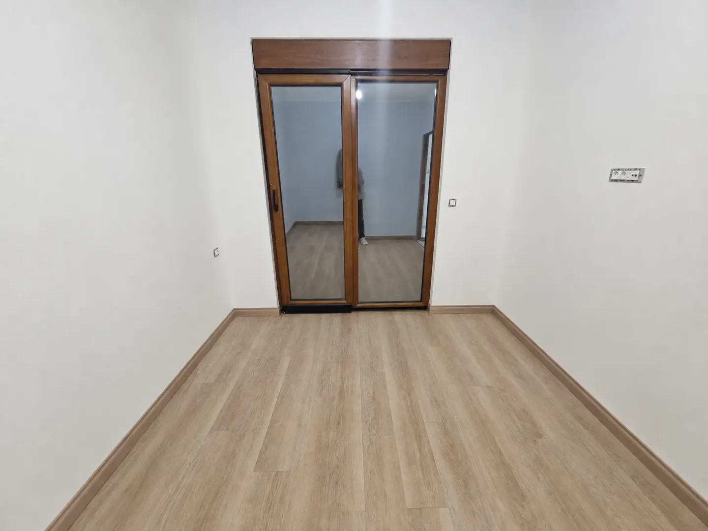 Prazna soba sa laminatom i balkonskim vratima.