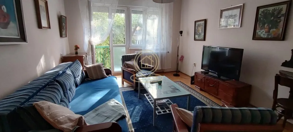 Dnevna soba sa garniturom, stočićem, televizorom i izlazom na terasu.