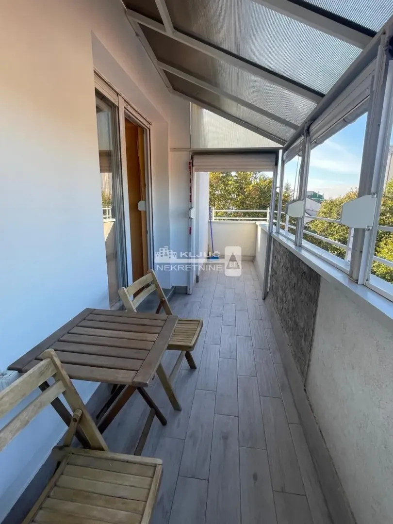 Zastakljeni balkon sa garniturom za sedenje i drvenim podom.