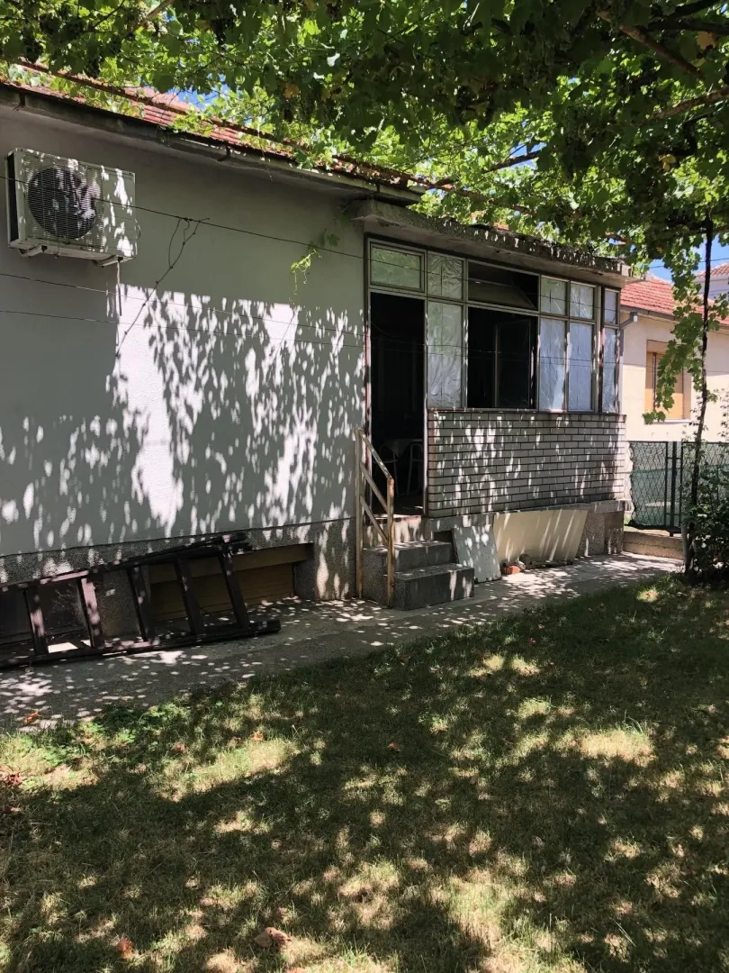 Spoljašnjost kuće sa dvorištem u sjenci drveća.