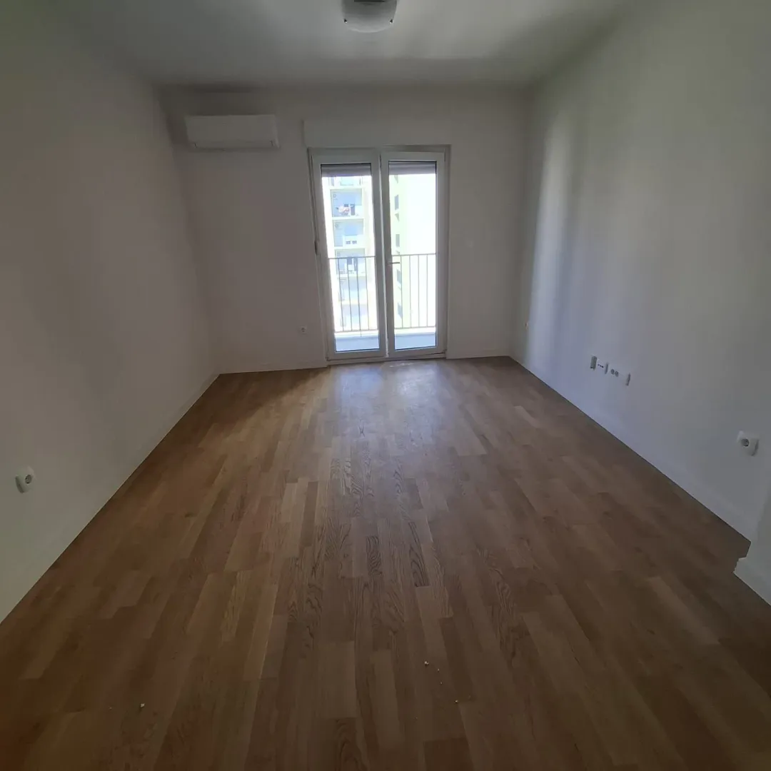Empty room with wooden flooring and balcony doors.