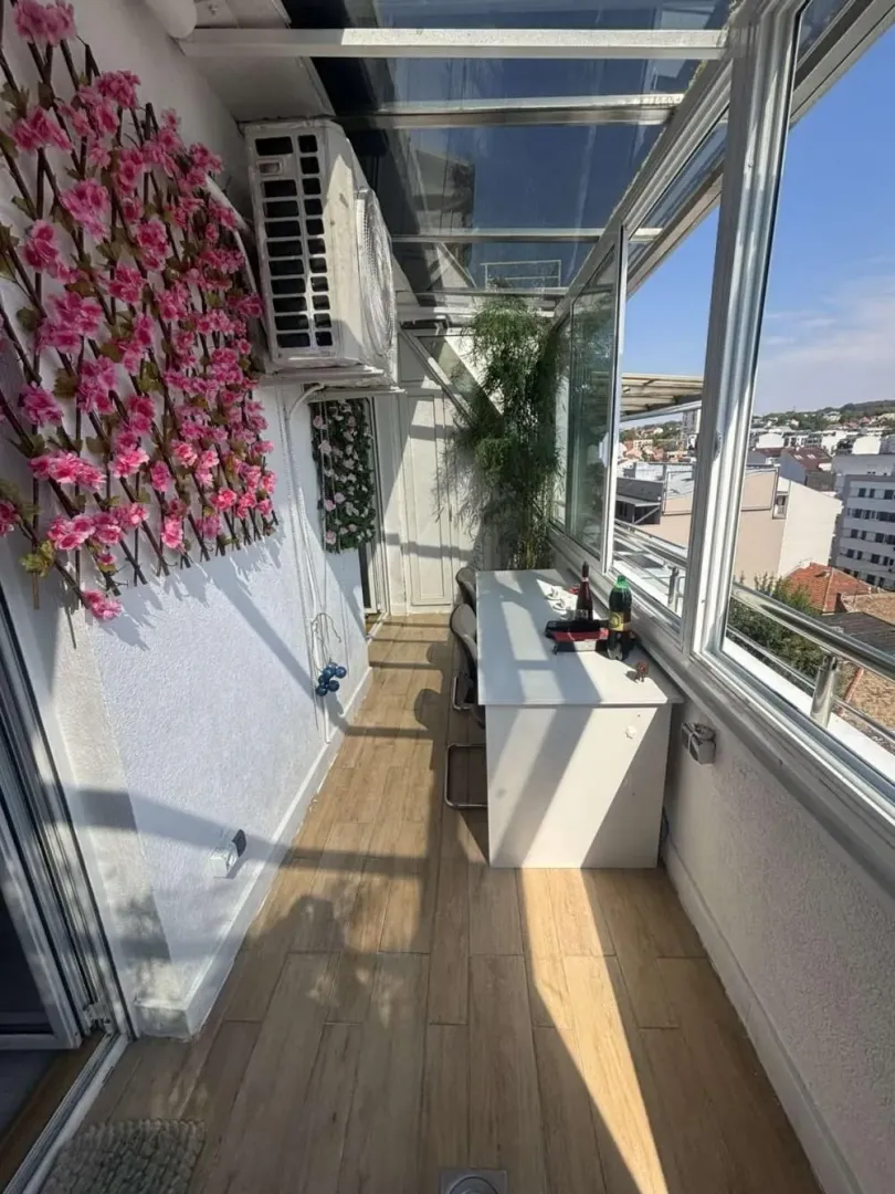 Enclosed balcony with a desk and decorative artificial flowers on the wall.
