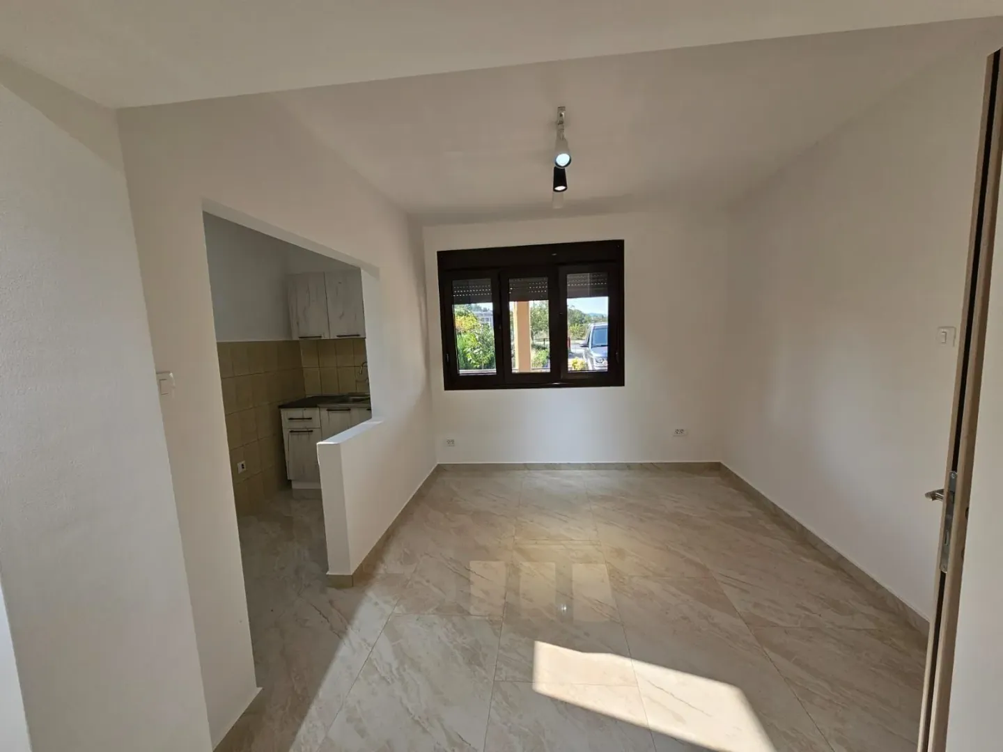 Bright empty room with tiled floors and a kitchen alcove.