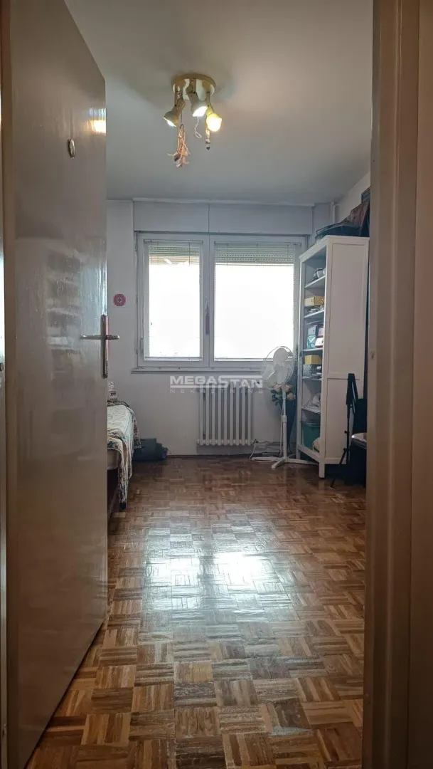 Pogled iz hodnika na nameštenu spavaću sobu sa prozorom i drvenim parketom.
