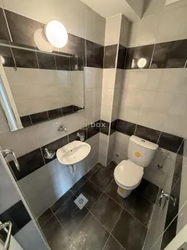 Small bathroom with a sink, mirror, and toilet, tiled with grey tiles. - image 5