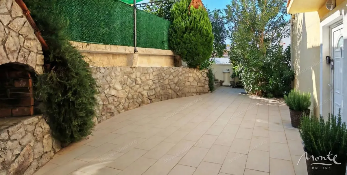 Popločano dvorište sa zidanim roštiljem i zelenilom.