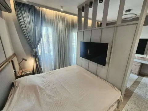 Modern bedroom with a double bed, TV mounted on a partition wall, and a large window with curtains. - image 7