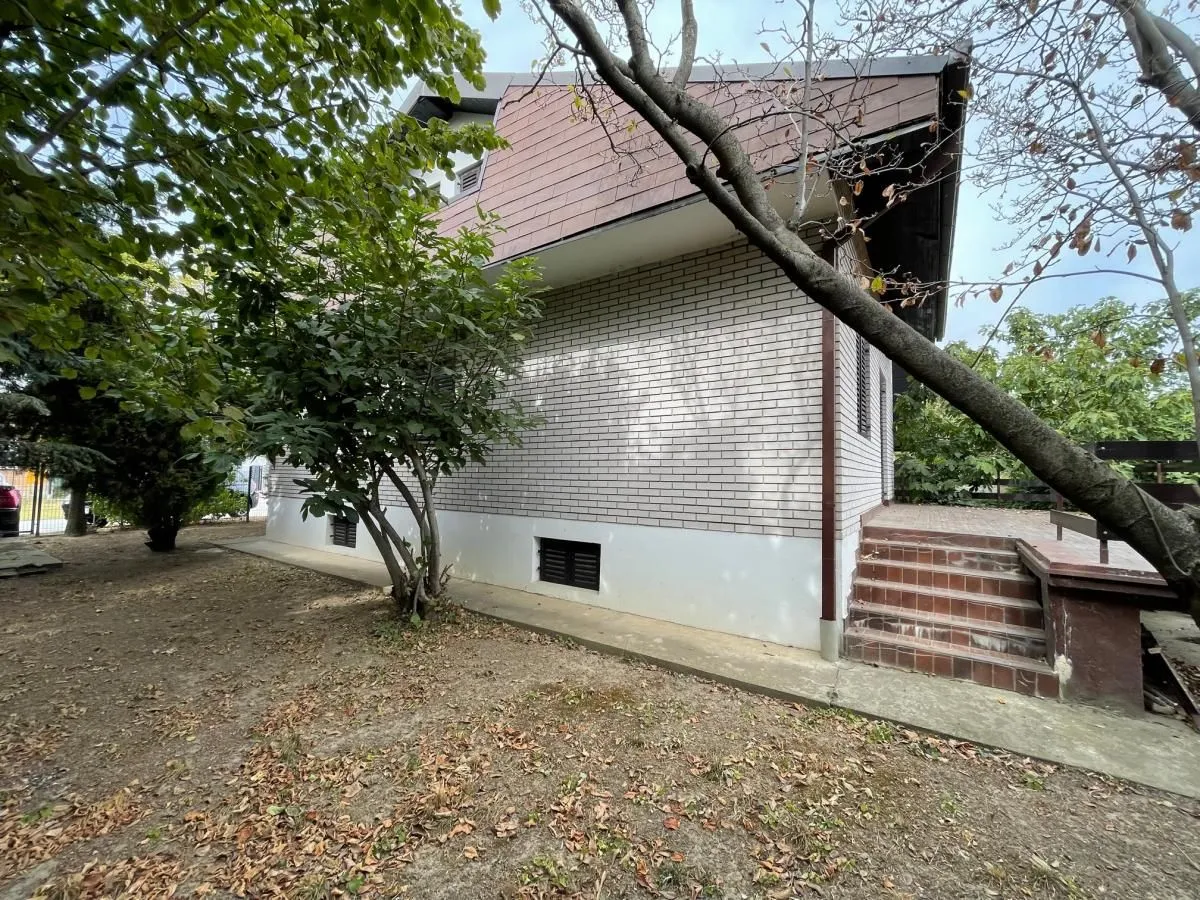 Bočni pogled na kuću sa dvorištem i drvećem.