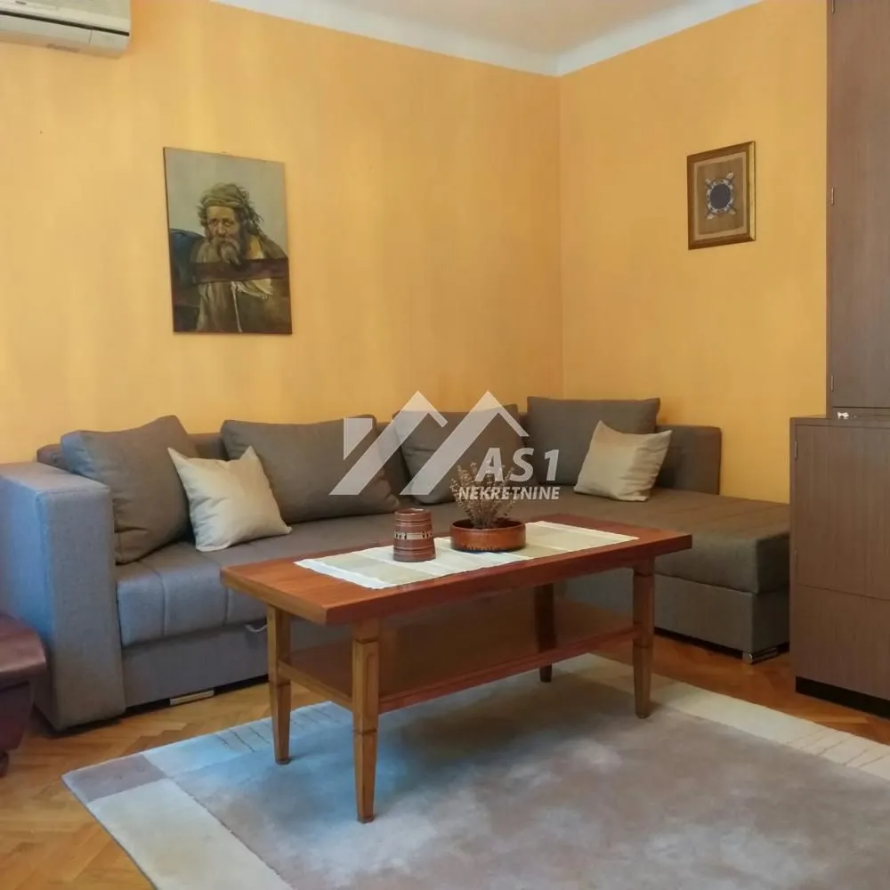 Dnevna soba sa ugaonom garniturom, drvenim stočićem i žutim zidovima.