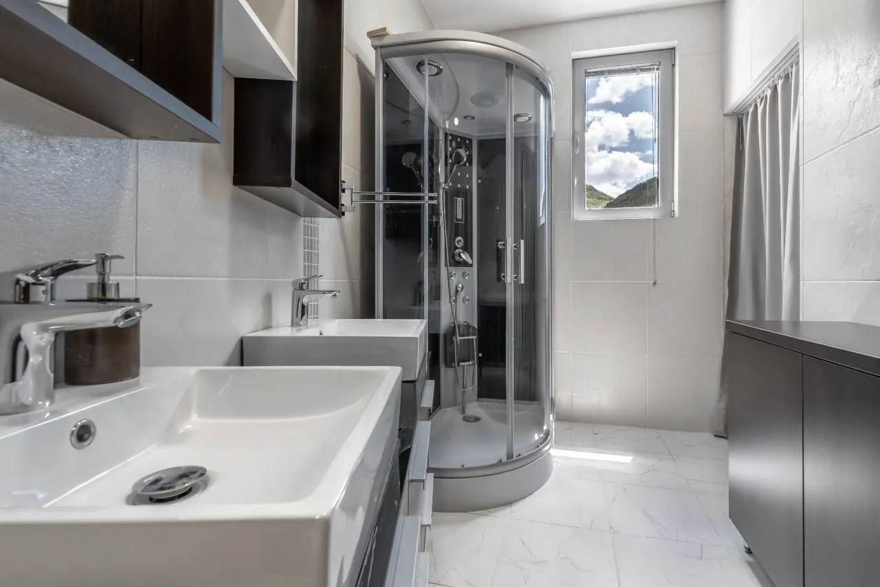 A modern bathroom equipped with a shower cabin and double washbasins.