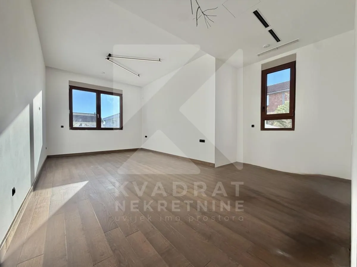 Empty room with white walls, wooden flooring and two windows.