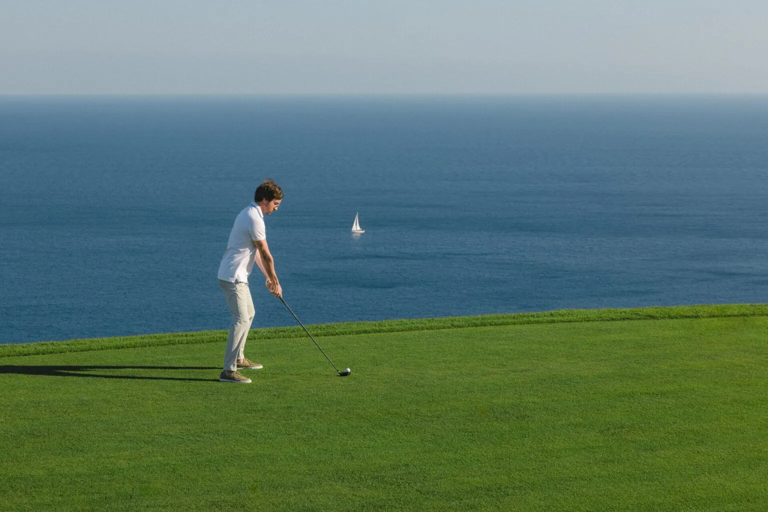 Travnjak sa pogledom na more i osobu koja igra golf.