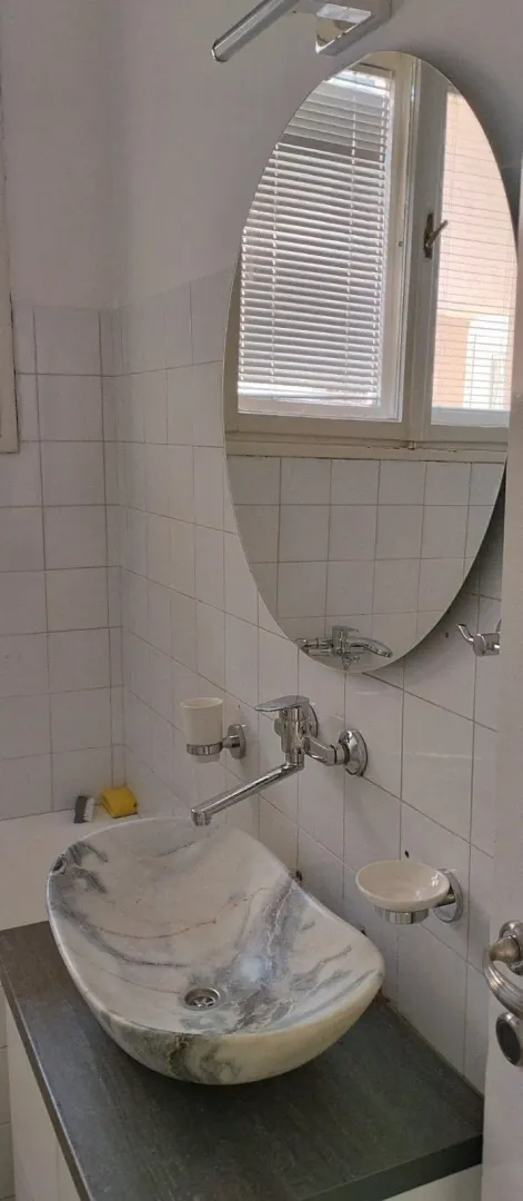 Kupatilo sa upečatljivim mermernim lavaboom i ovalnim ogledalom.