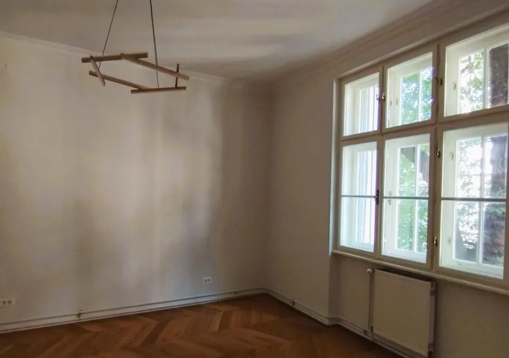 Empty room with parquet flooring and large windows.