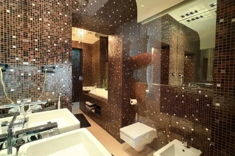 Modern bathroom covered with brown mosaic tiles featuring two sinks and a toilet. - image 13