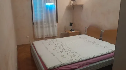 Jednostavna spavaća soba sa bračnim krevetom i noćnim ormarićem pored prozora. - image 6
