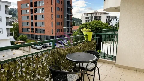 Namješten balkon sa stolom i stolicama i pogledom na okolne zgrade i parking. - image 6