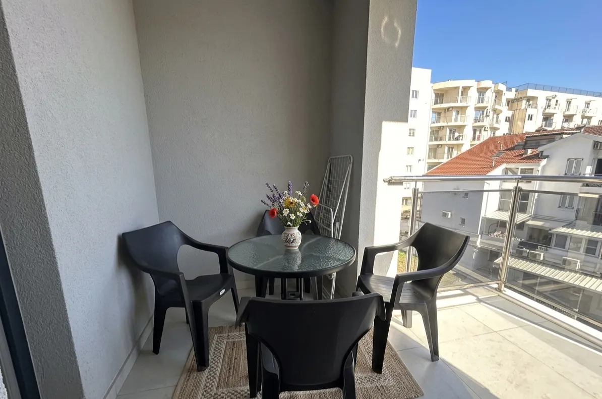 Manji namješteni balkon sa stočićem, stolicama i vazom sa cvijećem.