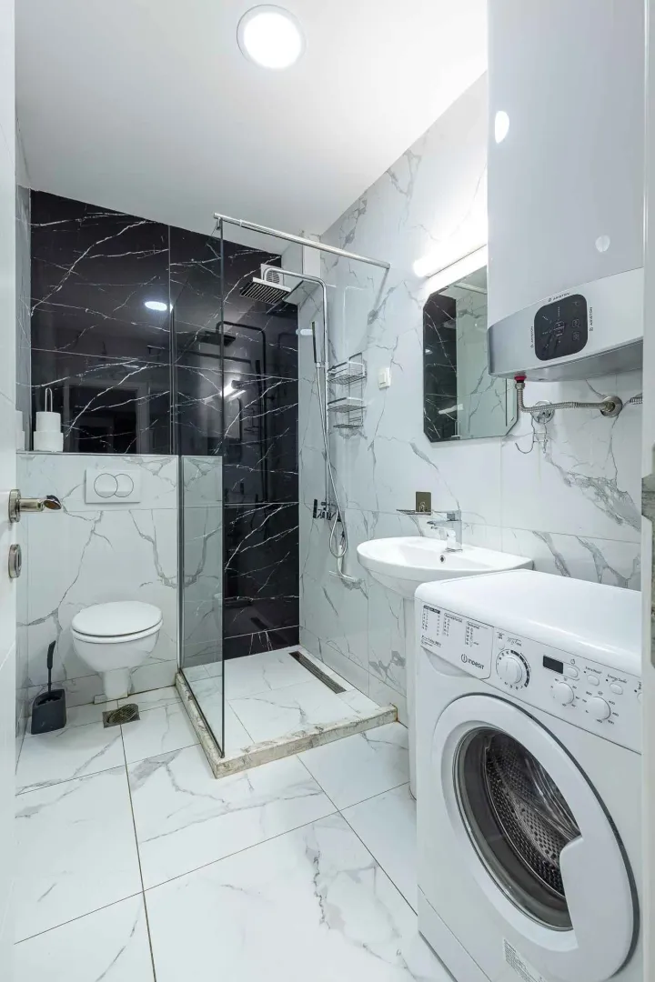 Modern bathroom with a shower cabin, washbasin, and washing machine.