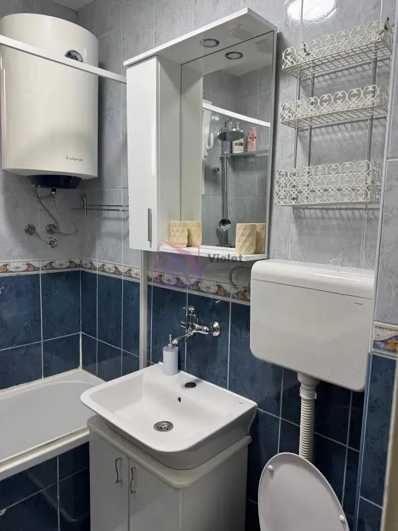 Manje kupatilo sa plavim i bijelim pločicama, umivaonikom, WC šoljom i bojlerom.