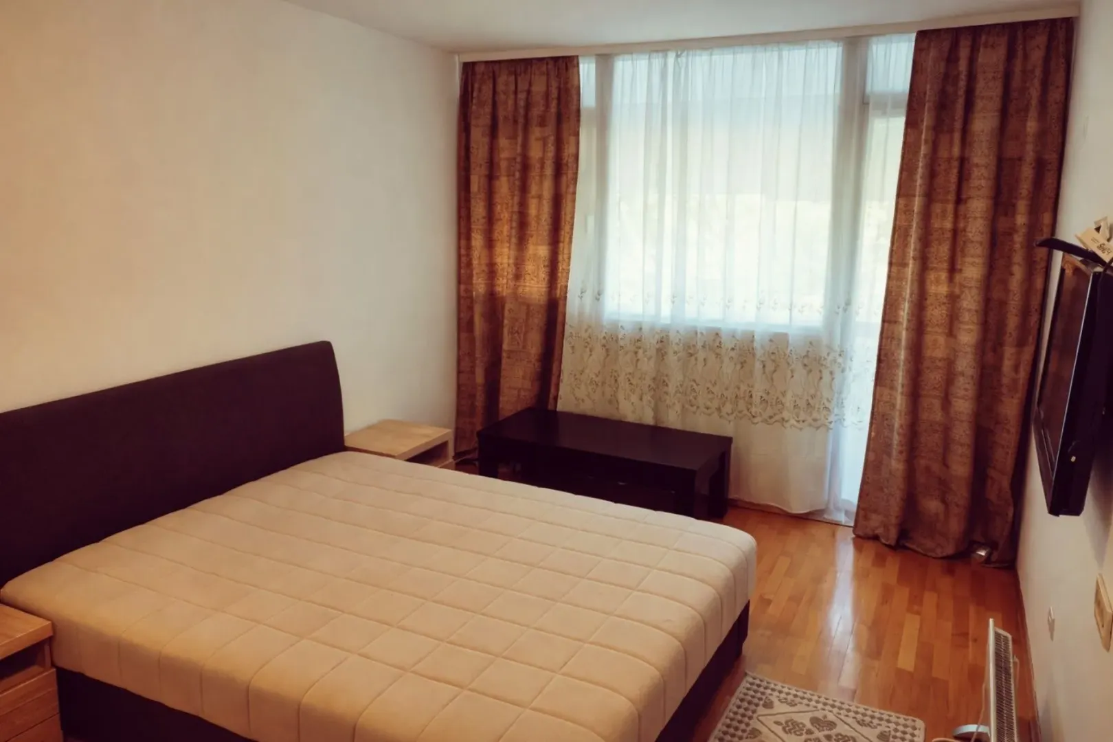 Svijetla spavaća soba sa bračnim krevetom, drvenim podom i prozorom.