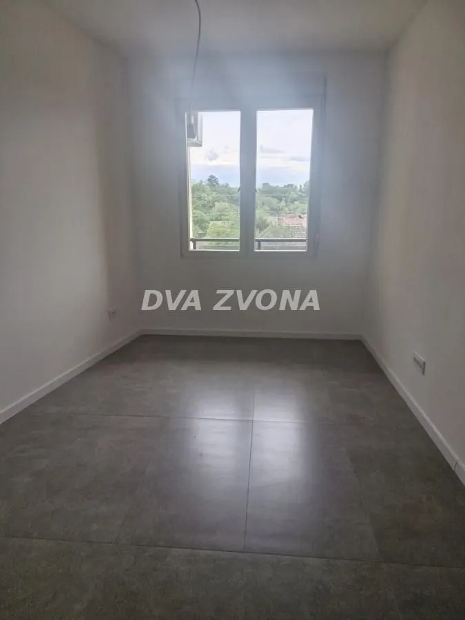 Prazna soba sa sivim pločicama na podu i prozorom.