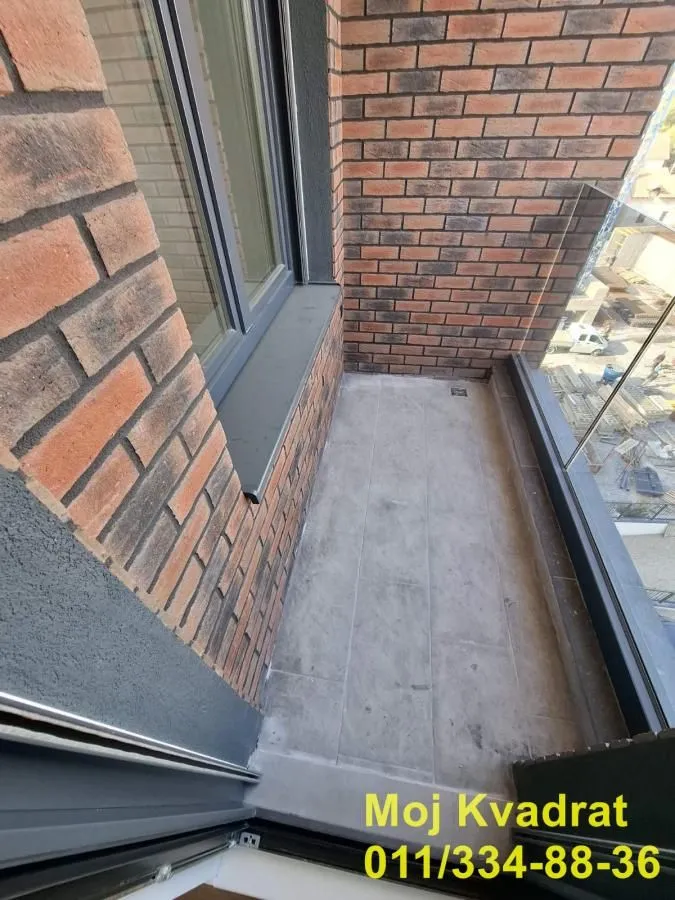 Manji balkon sa ciglenim zidom i staklenom ogradom.