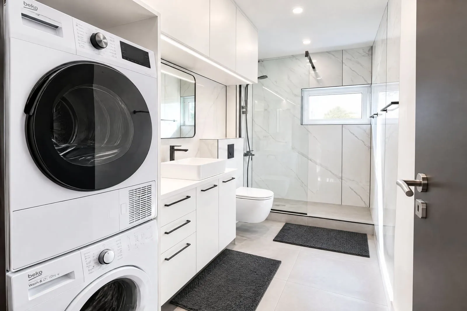 Modernly equipped bathroom with white fixtures, walk-in shower, and integrated washing machine.
