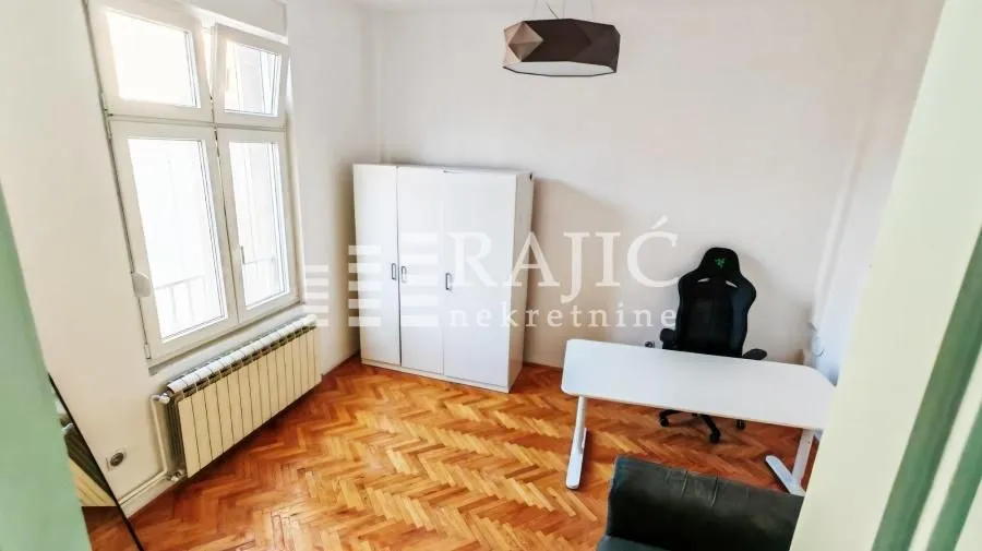 Prazna soba sa radnim stolom, stolicom i belim garderoberom.