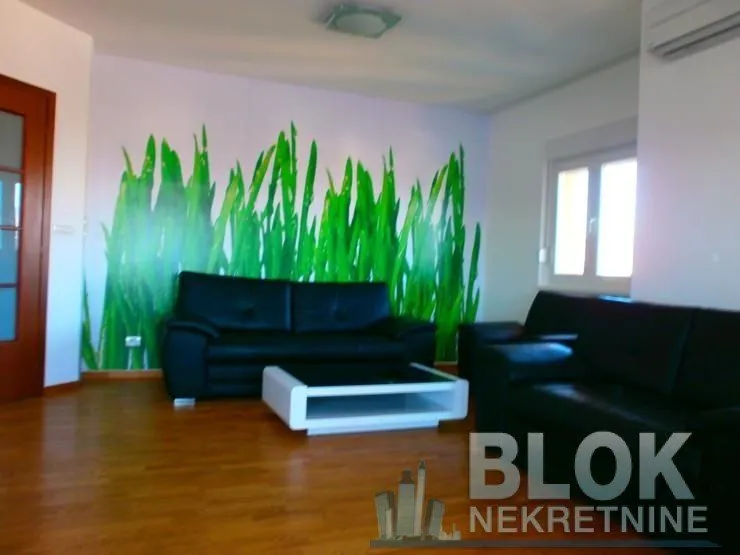 Living room with black leather sofas and grass-patterned wallpaper.