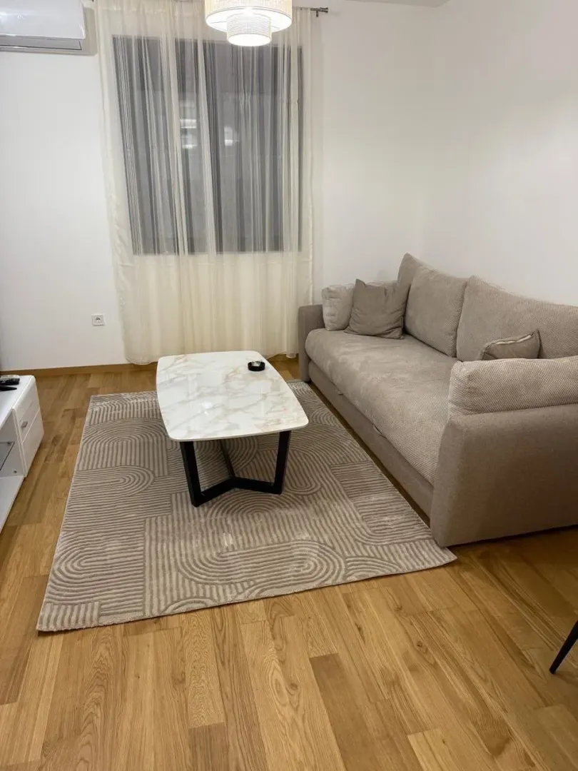 Dnevna soba sa ugaonom garniturom, klub stolićem i prozorom sa zavjesama.
