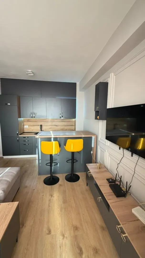 Moderna kuhinja sa šankom i žutim barskim stolicama, povezana sa dnevnim boravkom.