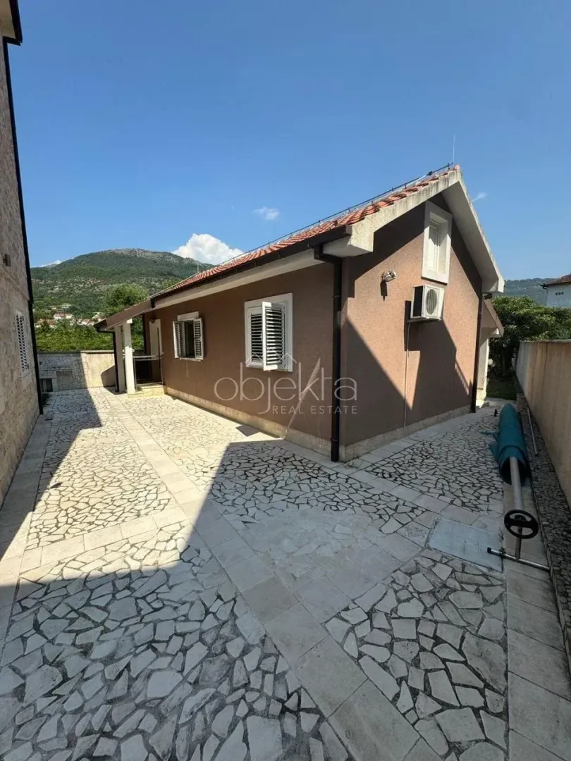 Bočni pogled na kuću sa popločanim dvorištem i pogledom na brda.