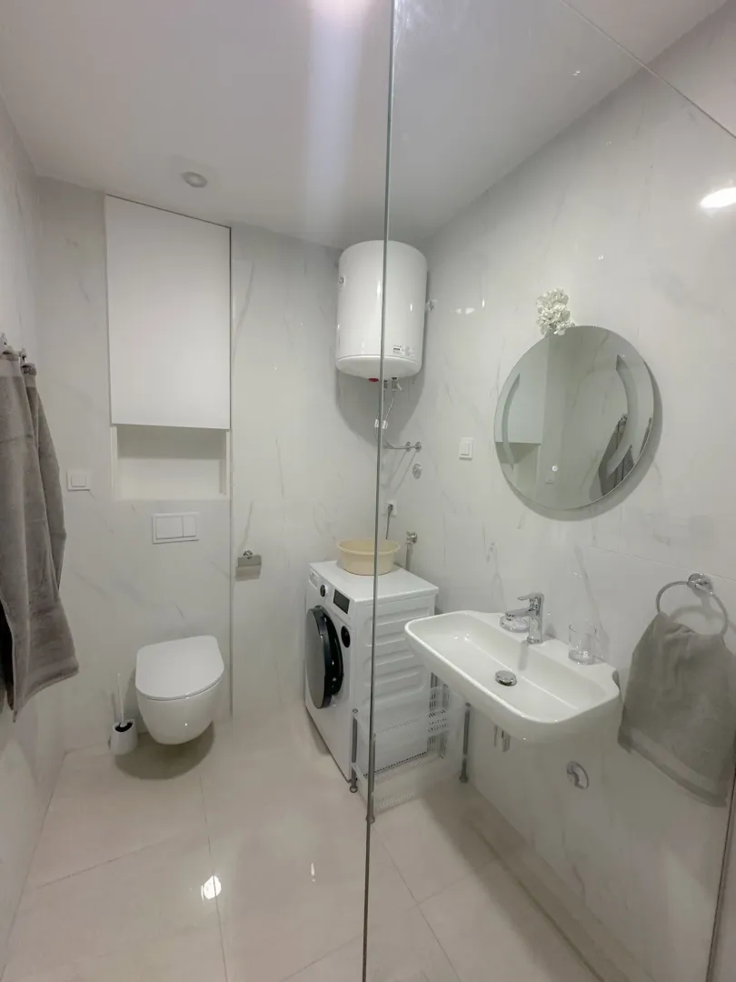 Svijetlo i moderno kupatilo sa veš mašinom i staklenom pregradom.