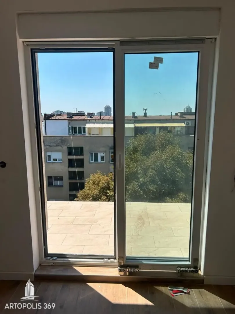 Pogled kroz prozor na okolne zgrade i gradski pejzaž.