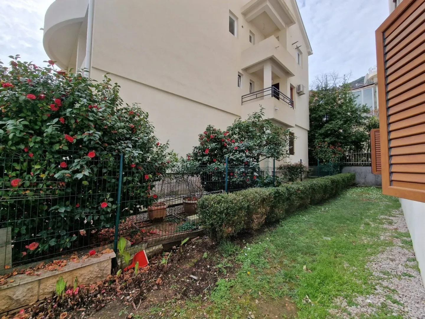 Pogled na dvorište i spoljašnjost zgrade sa uređenim zelenilom i ogradom.