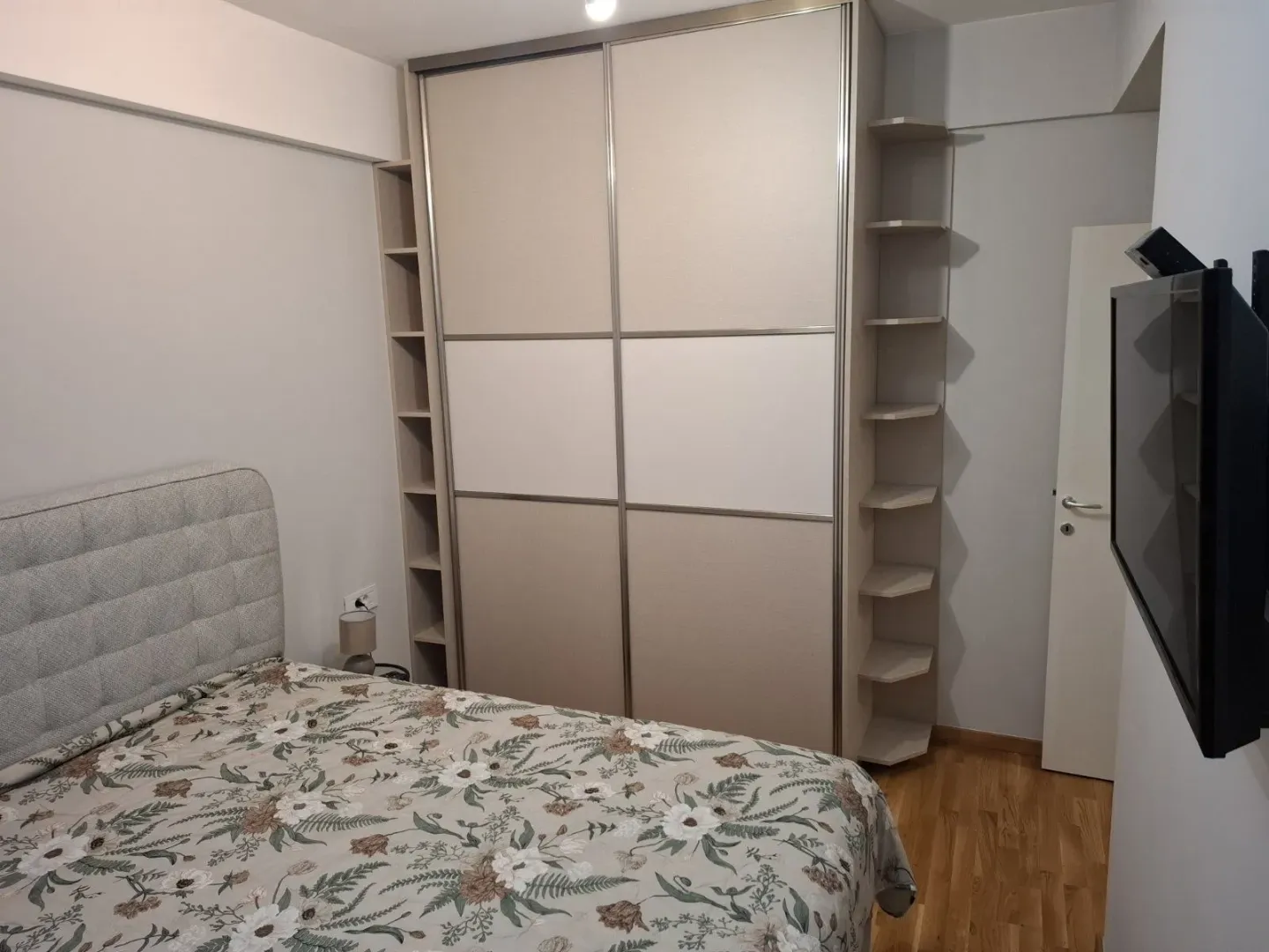 Spavaća soba sa bračnim krevetom, velikim garderoberom i televizorom na zidu.