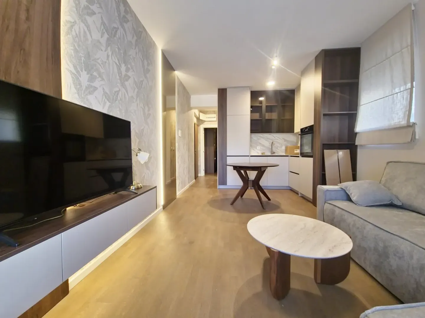 Living room with a sofa, TV, and an open kitchen with a dining table.
