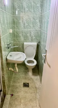 Manje kupatilo obloženo zelenim pločicama sa toaletom i umivaonikom. - image 8