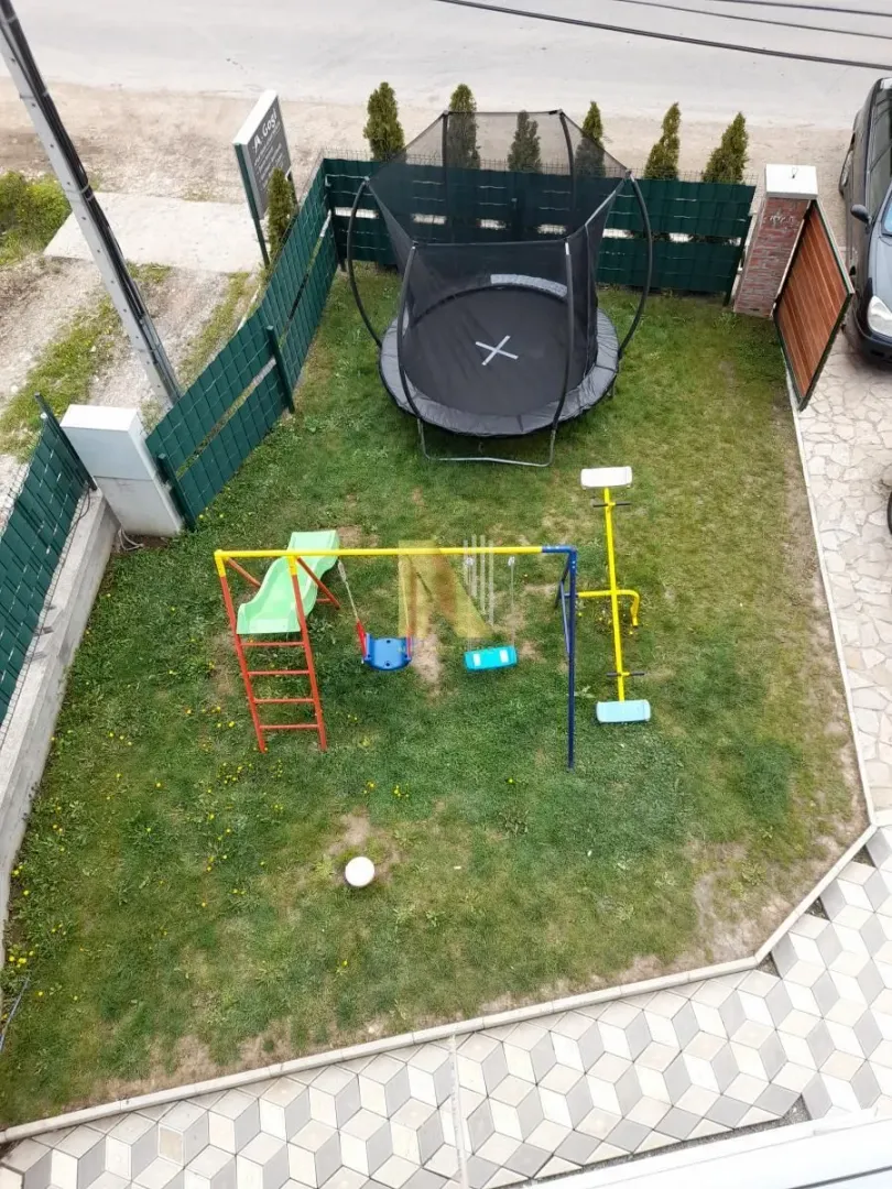 Top-down view of a fenced yard with a children's playground and trampoline.