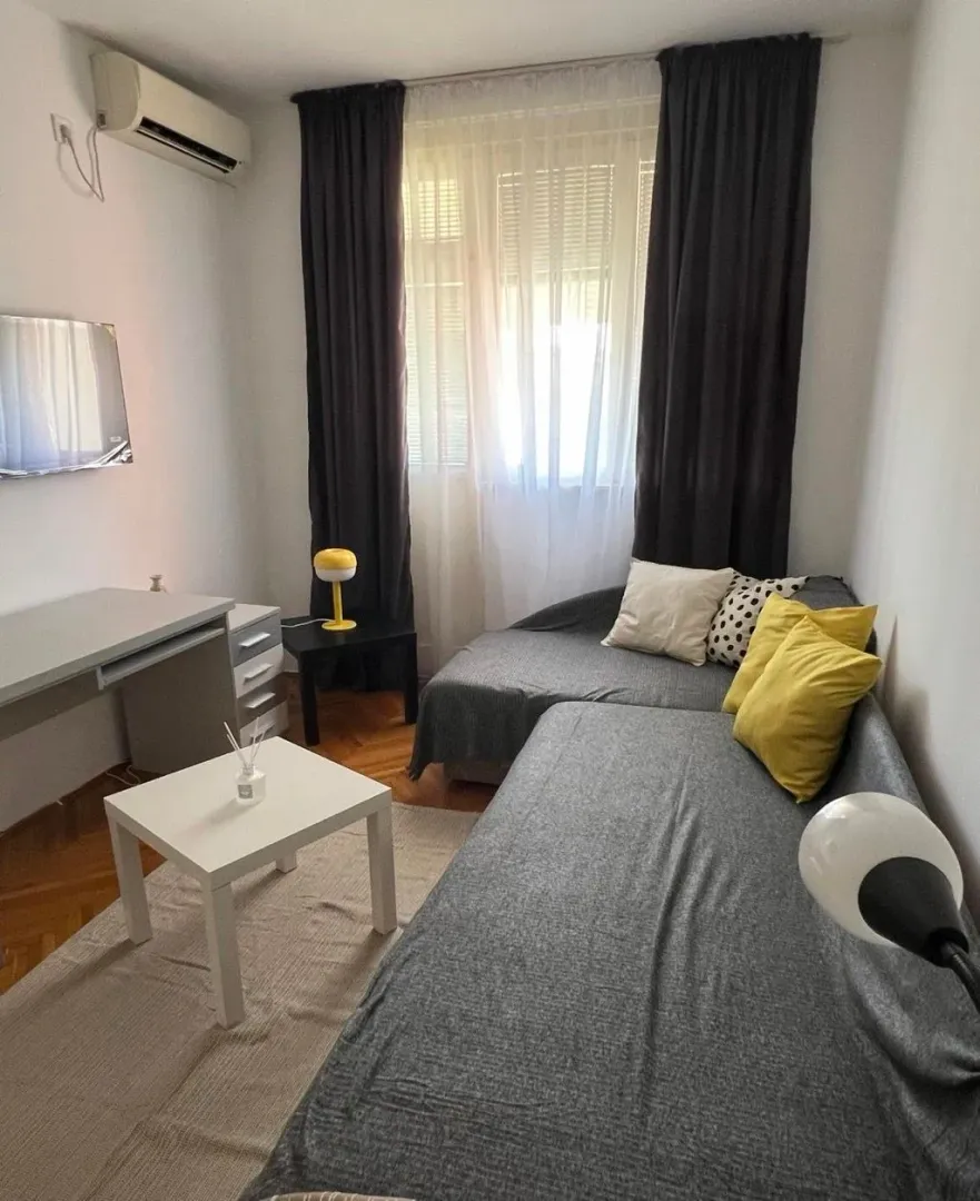 Small living room with a sectional sofa, desk, and air conditioning.