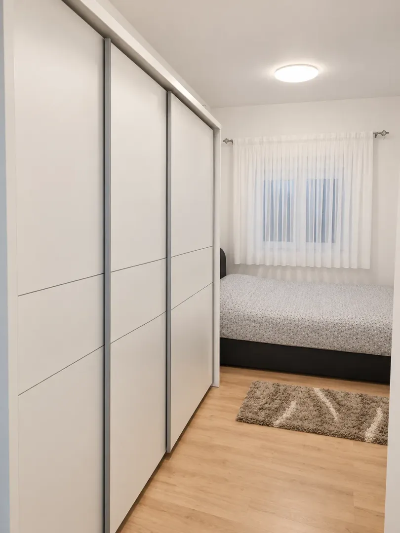 Manja spavaća soba sa velikim bijelim plakarom i krevetom.
