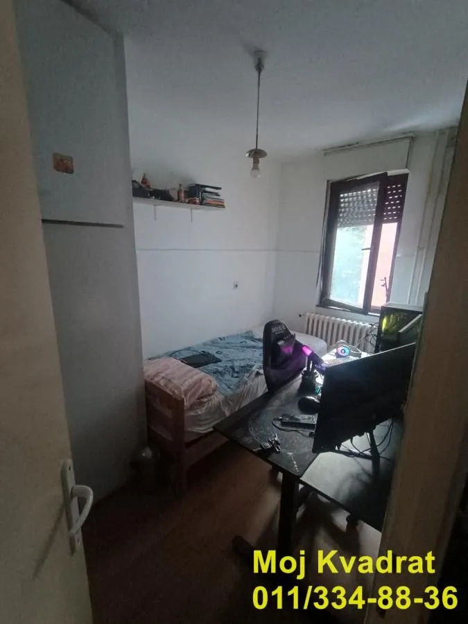 Manja spavaća soba sa krevetom i radnim stolom sa računarom.