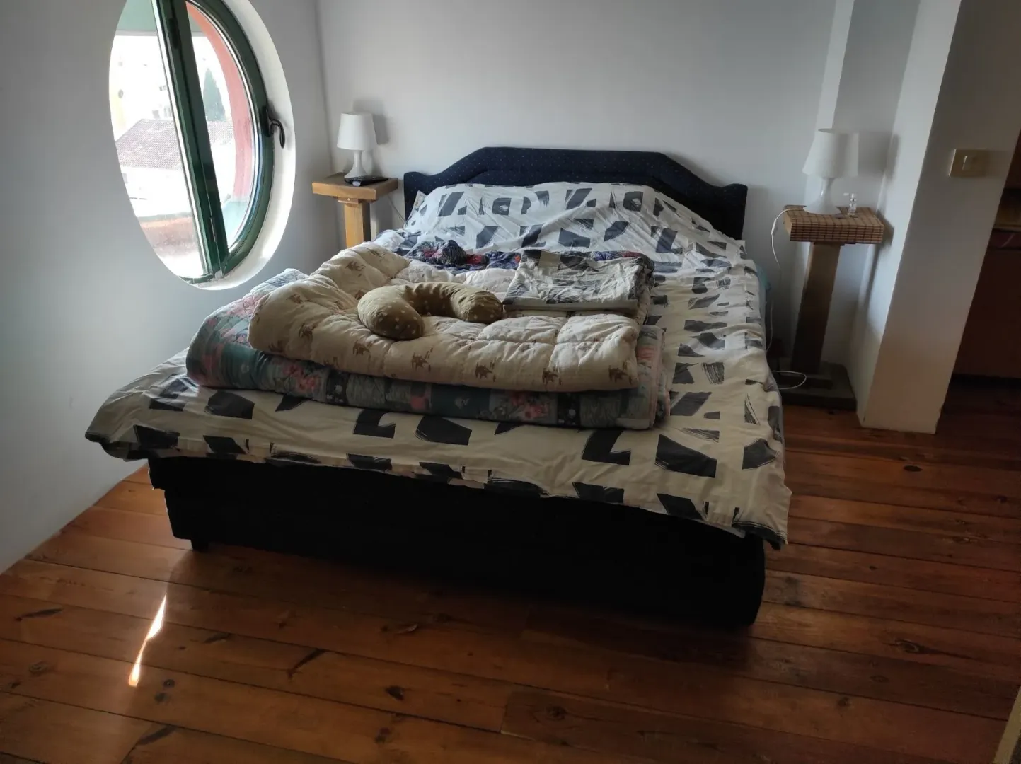 Bright bedroom featuring a round window and wooden flooring.