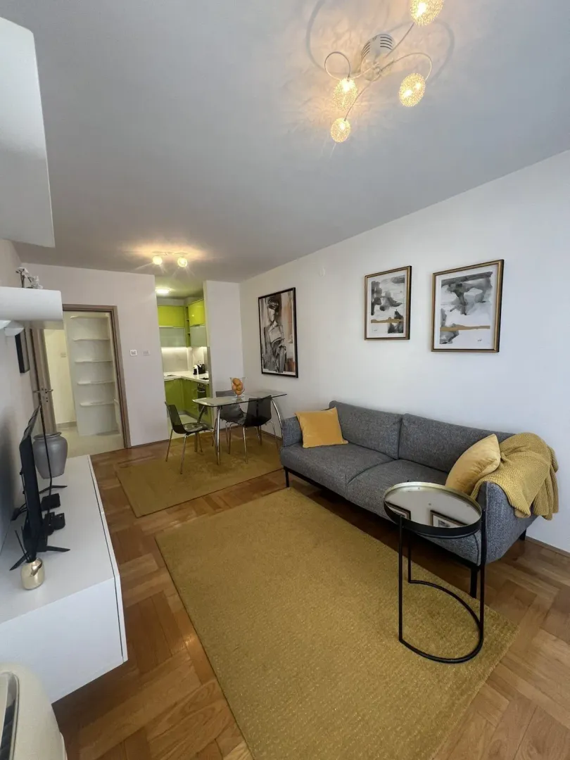 Bright living room with a grey sofa, dining table, and kitchen in the background.